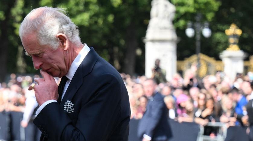 King Charles III looks solemn as a crowd looks on in the background